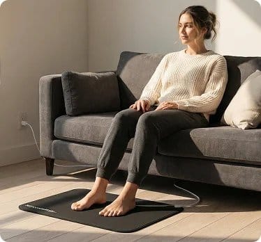 Woman sitting on couch using Terra Grounding Mat with bare feet